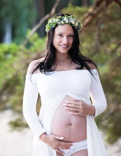 Schwangere Frau im weißen Bellykleid mit Blumenhaarkranz