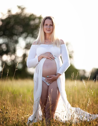 Schwangere Frau im weißen Bellykleid im Sonnenuntergang auf goldenem Feld